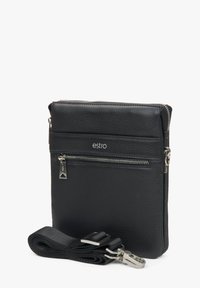 Černá kožená crossbody taška se strukturovaným povrchem, předními zipovými kapsami a stříbrnými prvky. Obsahuje nastavitelný popruh. Viditelné logo značky.