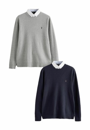 Two sweaters: one in light gray, one in dark navy. Both feature ribbed texture, crew necks, and a white collared shirt underneath. Icon on front.
