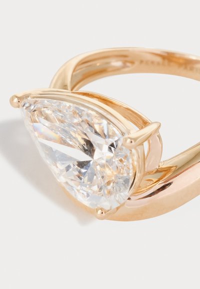 Inel de aur cu o piatră prețioasă transparentă mare, în formă de pară, fixată cu trei gheare pe o bandă netedă, pe un fundal deschis.