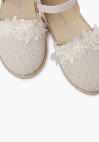Espadrilles en toile beige avec des accents de dentelle florale, un dessus texturé et une semelle en corde de jute. Comprend une sangle de cheville réglable pour un maintien sécurisé.