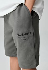 Grå bomullsshorts med sidfickor, med trycket "ALLSAINTS" i svart. Slät textur och avslappnad design, lämplig för vardagsbruk.