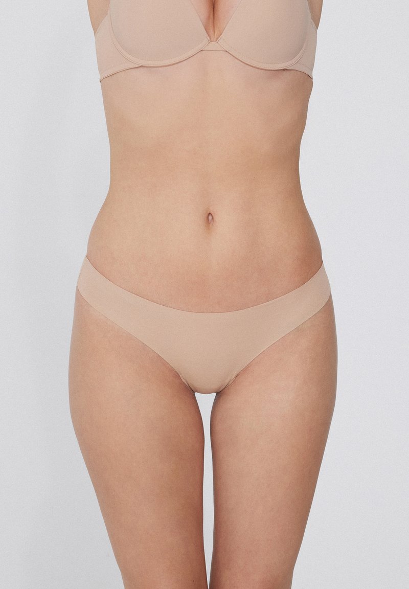 Nackte, nahtlose Bikini-Unterwäsche mit niedriger Leibhöhe, gefertigt aus glattem Stoff. Verfügt über ein minimalistisches Design und einen weichen Elastikbund.