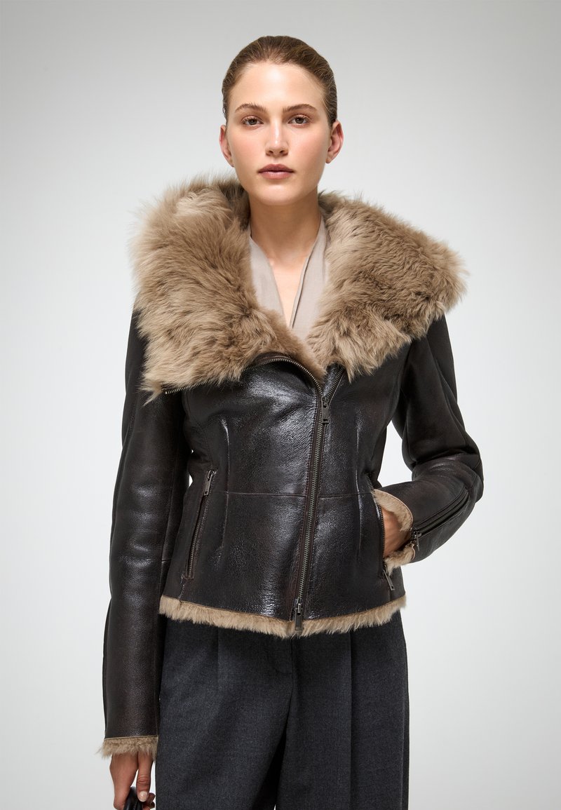 Braune Lederjacke mit einem plüschigen, hellbraunen Futterkragen und Besatz. Verfügt über einen Reißverschluss vorne und seitliche Taschen. Glatte Textur, taillierter Schnitt.