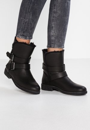 Svarta ankellånga stövlar i läder med en mjuk pälsfoder. Har två justerbara remmar och en strukturerad gummisula.