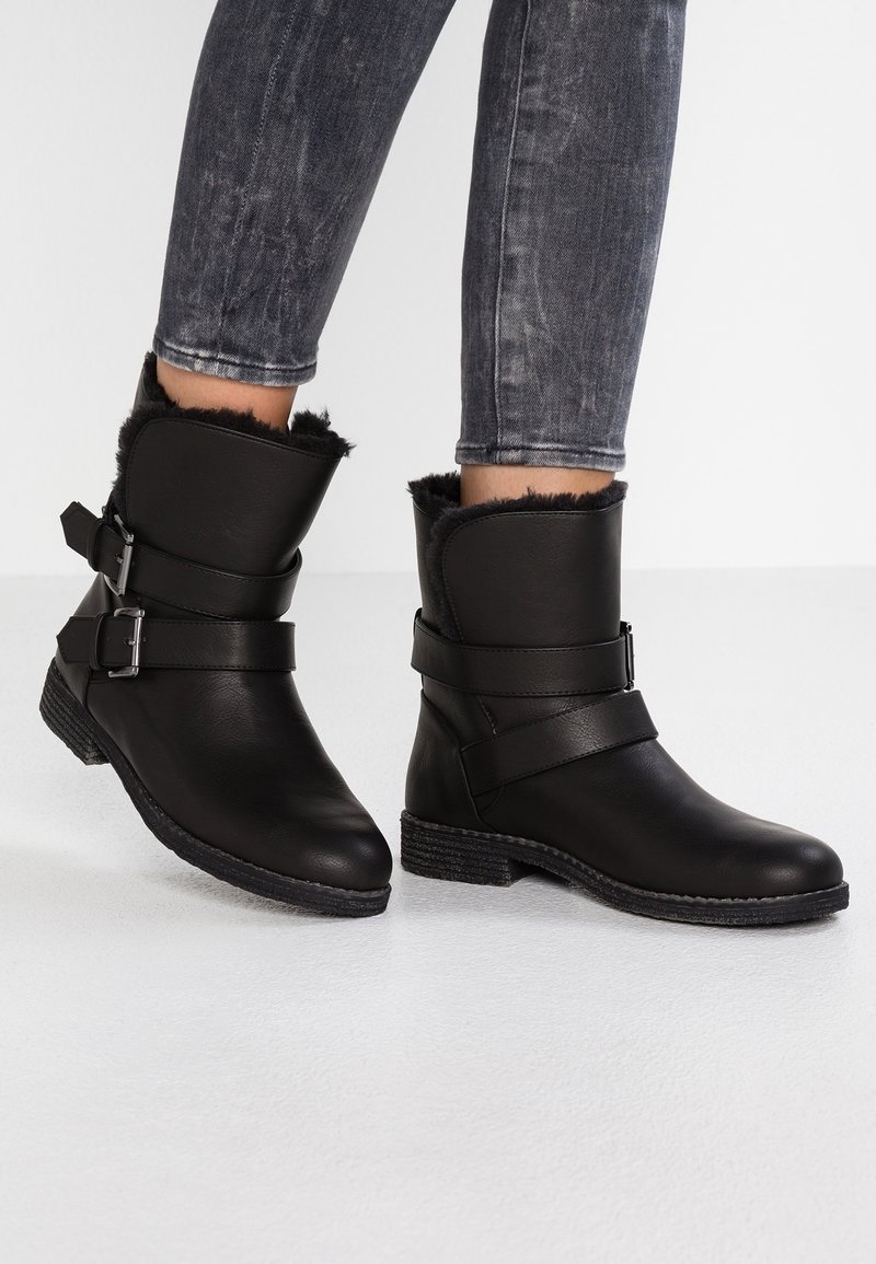 Botas de tobillo negras de cuero con un suave forro de piel. Cuentan con dos correas ajustables y una suela de goma texturizada.