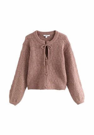 Femme portant un cardigan rose poussiéreux texturé avec des boutons en forme de cœur, un pantalon en cuir noir large et court, et des talons slingback noirs à bout pointu.