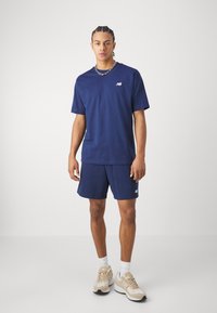T-shirt en coton bleu marine à manches courtes et col rond, associé à un short assorti. Logo blanc sur la poitrine et sur le short. Baskets neutres.