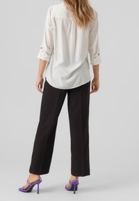Camicia bianca con bottoni e maniche arrotolate, abbinata a pantaloni neri a gamba larga e sandali con tacco alto viola. Tessuto dalla superficie liscia.