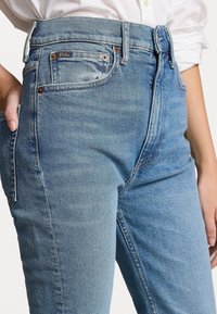 Ljusblå denimjeans med hög midja, klassisk femfickdesign och subtila färgavvikelser. Har metallbeslag och kontrasterande sömmar.