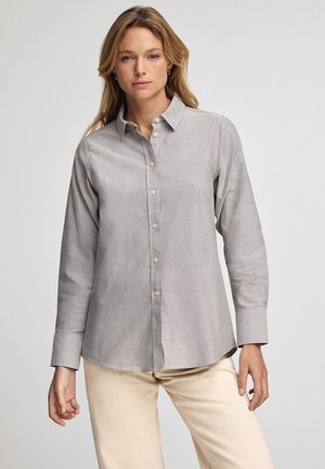 Camicia grigia chiara con bottoni, maniche lunghe, colletto a punta e orlo dritto. Realizzata in un tessuto morbido e strutturato con bottoni beige.