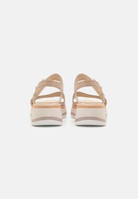 Beige sandals with cross-strap design, soft leather texture, and a stacked platform sole featuring a subtle color gradient. Adjustable ankle strap.