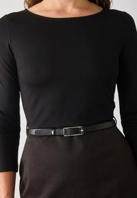 Zwarte lange mouwen top met een bateauhals, gecombineerd met een strakke, donkerbruine rok die is vastgemaakt met een smalle zwarte leren riem met een zilveren gesp.