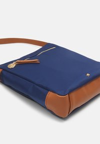 Námořnická látková taška přes rameno s hnědými koženými akcenty, zipovou kapsou a zlatými kovovými prvky. Hladký povrch, obdélníkový tvar a nastavitelné popruhy.