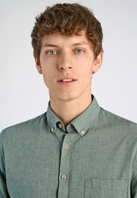 Camisa de botones verde claro hecha de un tejido texturizado, con cuello, bolsillo frontal y detalles de botones en la tapeta.