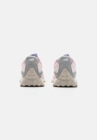 Un paio di scarpe da ginnastica New Balance rosa e grigie viste da dietro, che evidenziano le suole beige testurizzate con motivi circolari.