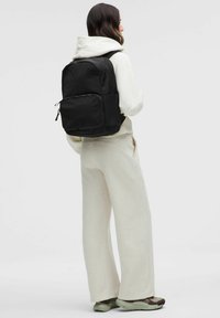 Zwarte rugzak met een elegant ontwerp, gemaakt van duurzame stof, met een voorkant met ritszak, verstelbare riemen en minimalistische accenten.