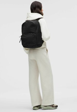 Musta reppu, jossa on tyylikäs muotoilu, valmistettu kestävästä kankaasta, etulokerossa on vetoketju, säädettävät hihnat ja minimalistiset yksityiskohdat.