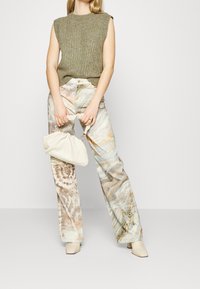 Olijfgroen gebreid mouwloos topje gecombineerd met marmerpatroon wijde broek in beige en lichtblauw. Geaccessoireerd met een crèmekleurige clutch.