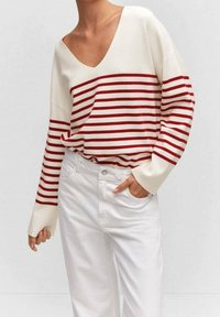 Punainen ja valkoinen raitapaita, jossa on syvä V-pääntie ja pitkät hihat, yhdistetty valkoisiin farkkuihin. Ominaisuutena rento istuvuus.