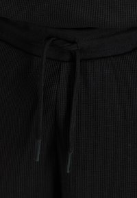 Gros plan sur la ceinture en tissu côtelé noir d'un pantalon de survêtement avec un cordon noir noué.
