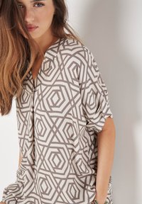 Kurzärmlige Bluse mit einem geometrischen Muster in Beige- und Brauntönen. Sie hat einen V-Ausschnitt und eine lockere Passform und ist aus einem glatten, leichten Stoff hergestellt.