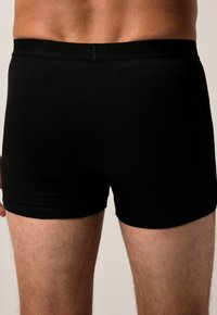 Boxeurs en coton noirs avec une texture lisse, dotés d'une ceinture élastique noire avec un logo. Longueur de jambe courte et design ajusté.