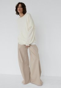 Oversize kremowy sweter z długimi rękawami, zestawiony z szerokimi beżowymi spodniami. Gładka faktura i neutralna paleta kolorów.
