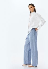 Wit overhemd met knopen en een relaxte pasvorm, lange mouwen, gecombineerd met lichtblauwe wijde broek met een elastische tailleband.