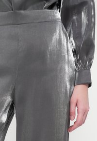 Hallgray metallik blouse, millel on sile tekstuur, pikad varrukad ja kokku tõmmatavad mansetid, peene läike ja õmbluste detailidega.