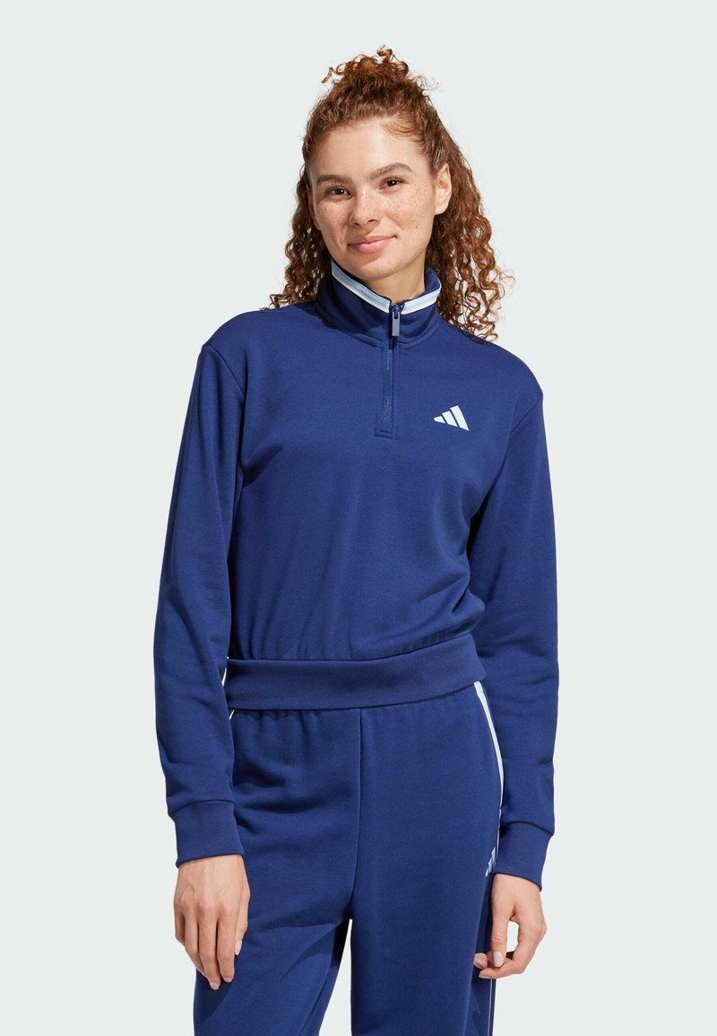 Mörkblå zip-up hoodie med hög krage, ribbstickade ärmslut, elastisk midja och vitt Adidas-logotyp på bröstet. Mjuk, sportig design.