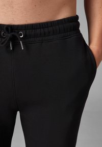 Schwarze Jogginghose mit Kordelzug, elastischem Bund und Seitentaschen, die eine glatte Textur und ein minimalistisches Design aufweist.