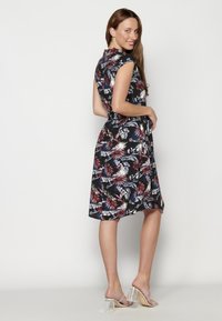 Rochie A-line florală de culoare neagră, cu modele în nuanțe de roșu, albastru și alb. Mâneci scurte și o curea la talie. Purtați cu sandale cu toc transparent.
