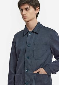 Marinblå knappad jacka med fyra knappar, bröstficka och två framfickor; tillverkad av texturerat tyg.