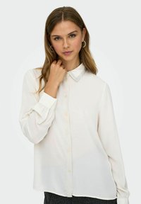Chemisier blanc à boutons avec un col bleu clair et des manches longues, fabriqué dans un tissu lisse et léger. Présente des poignets froncés et des boutons.