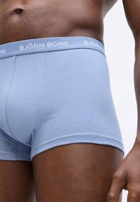 Κοντινό πλάνο ενός ατόμου που φοράει ανοιχτό μπλε μποξεράκια Björn Borg, δείχνοντας τη μέση και την άνω περιοχή του μηρού σε λευκό φόντο.