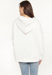 Witte oversized hoodie met een trekkoordkap, voorzien van elastische manchetten en een rechte zoom, gecombineerd met lichtblauwe denim jeans.