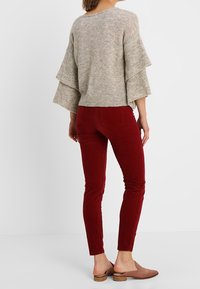 Pull gris clair en maille avec manches évasées superposées, associé à un pantalon en velours côtelé bordeaux slim et des chaussures marron à enfiler.