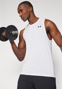 T-shirt de sport sans manches blanc avec un logo noir, porté par une personne soulevant un haltère noir. Tissu lisse, design ajusté et sans motifs visibles.
