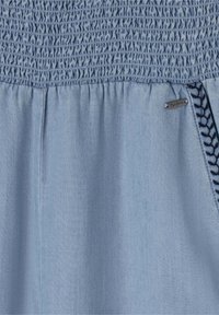 Modrý top s nařasením, vyrobený z texturované látky, s elastickým živůtkem a bočním detailem s černým vzorovaným akcentem. Připojena malá logo nášivka.