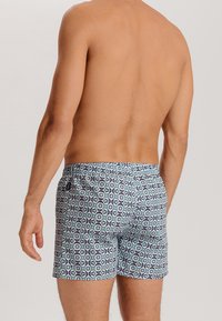Shorts de bain bleu clair avec un motif géométrique bleu foncé et blanc, dotés d'une taille élastique et d'un cordon de serrage.