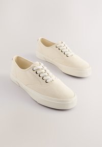 Kedai iš drobės, šviesiai balti, su žemu profiliu, apvaliais raišteliais, metalinėmis anga ir tekstūruotu guminės pado paviršiumi.