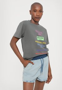 Grå kortermet t-skjorte med flerfarget logo-tekst på forsiden, kombinert med lyseblå denimshorts med snor i midjen.