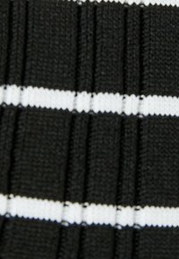 Svart tyg med horisontella vita ränder, som har texturerade åsar. Ränderna växlar i storlek och skapar en mönstrad effekt.