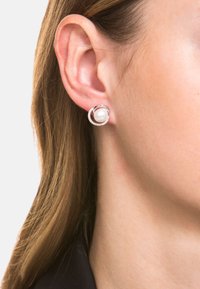 Pendientes de plata con una perla blanca redonda en el centro, rodeada por un aro circular adornado con pequeñas piedras transparentes.
