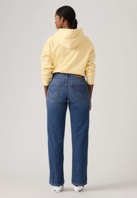 Κίτρινο φούτερ με κουκούλα, μπλε τζιν παντελόνι με πίσω τσέπες, άνετη εφαρμογή και ξεφτισμένο στρίφωμα. Μινιμαλιστικός σχεδιασμός με κλασικές λεπτομέρειες. Άσπρα αθλητικά παπούτσια.