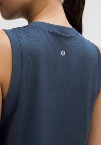 Majica brez rokavov v modri barvi za šport, izdelana iz teksturirane tkanine, z perforiranimi ploščami za zračenje ter majhnim logotipom na hrbtni strani.