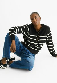 Black and white striped sweater with a henley collar and button detail, paired with light blue jeans and black sneakers with white stripes.