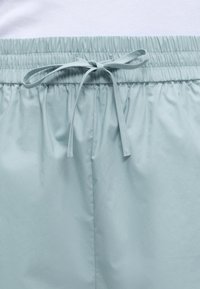 Ανοιχτό μπλε ελαστική μέση με δεμένη φιόγκο σε λείο ύφασμα, που δείχνει το πάνω μέρος φαρδιών παντελονιών ή σορτς.