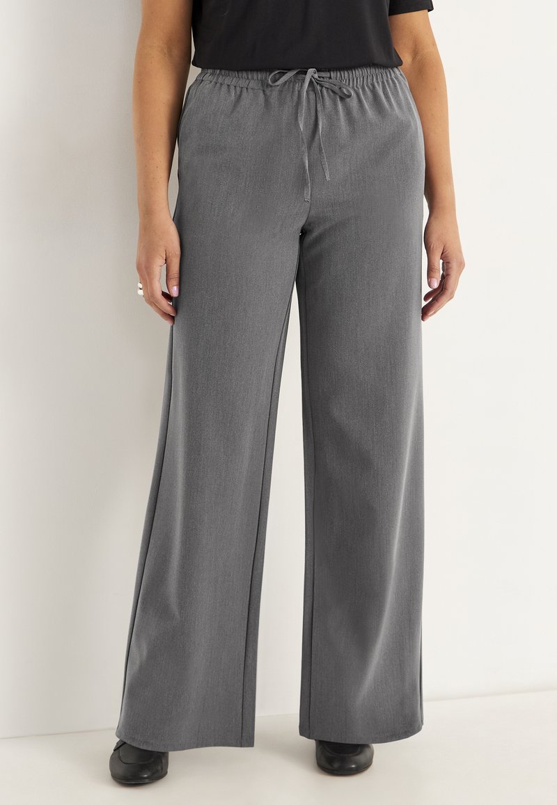 Grijze wijde broek met een elastische tailleband en koord, gemaakt van een zachte, gestructureerde stof, gecombineerd met zwarte schoenen.