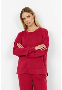 Hanorac roșu cu mânecă lungă, guler rotund, croială relaxată și textură striată. Asortat cu pantaloni roșii corespunzători, oferind un look coeziv.